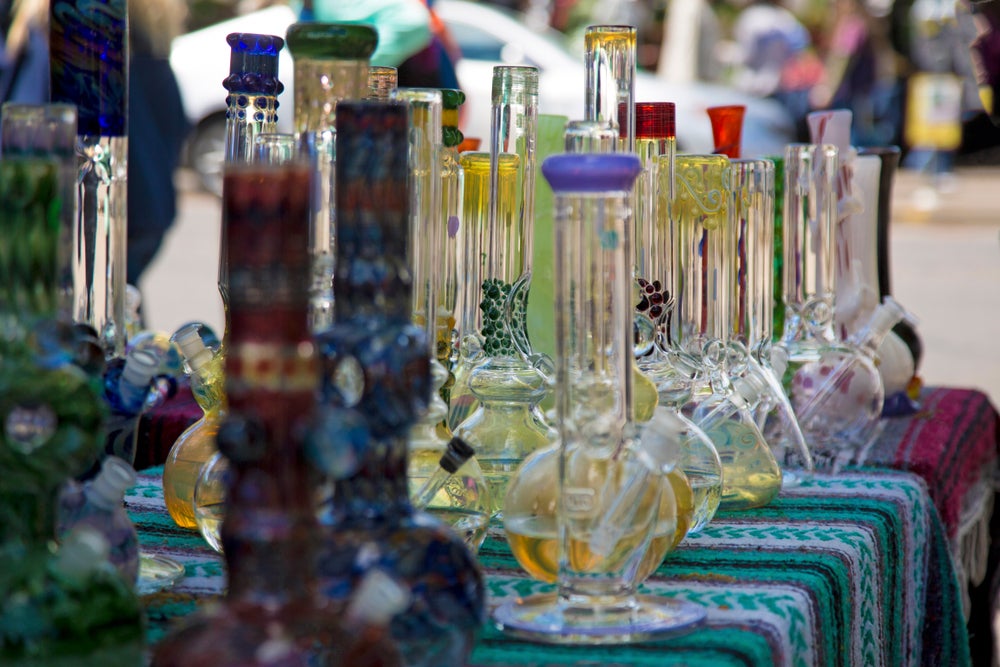 Bong stall at a 420 event. More than 20 different bongs are placed alongside each other over a carpet-draped table.