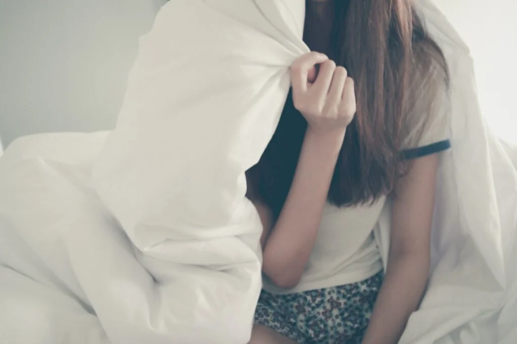 Young woman wrapped around by a white blanket.