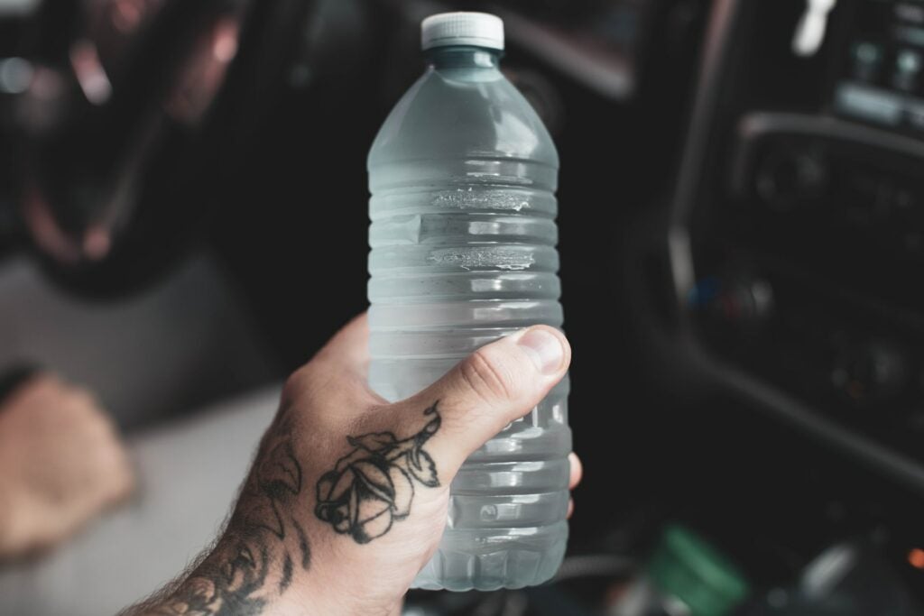 A guy with a tattoo holding onto a bottle of water.