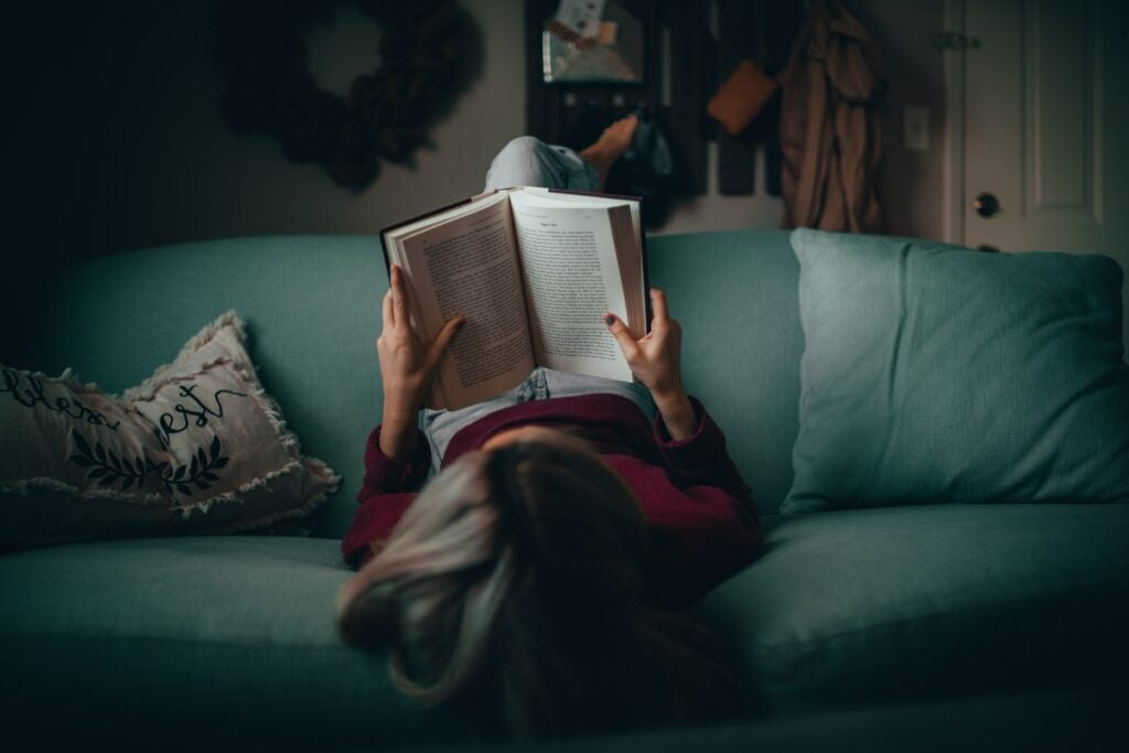 Girl on green sofa, lying upside down while reading a educational book.