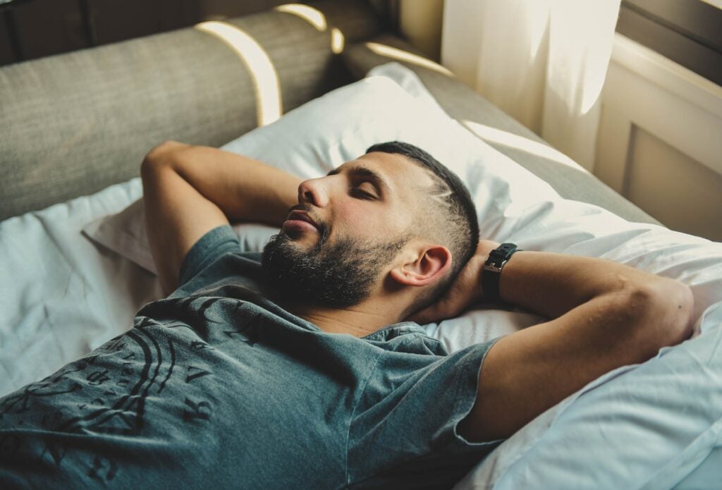 Young man resting on his bed with his head resting on his arms.