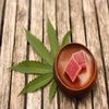 Edibles on a brown wooden plate placed next to a single cannabis leaf.