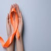 Two hands holding an orange ribbon that represents multiple sclerosis.