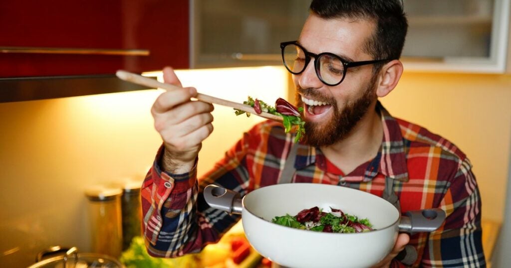 Young Caucasian man eating salad using a spatula.