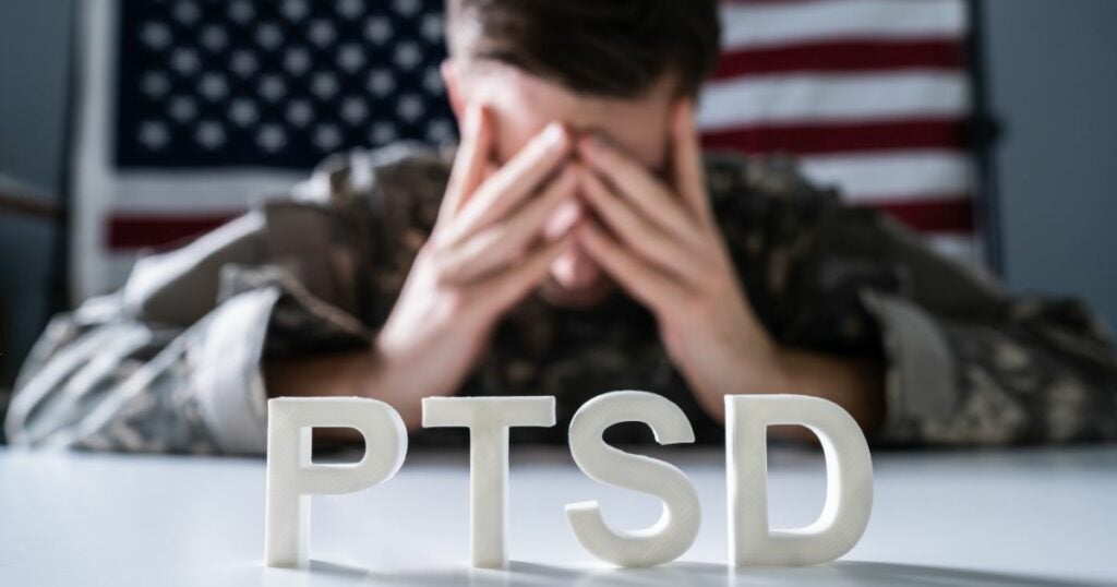 Young military man suffering from PTSD. He has his face in his hands and is looking down.