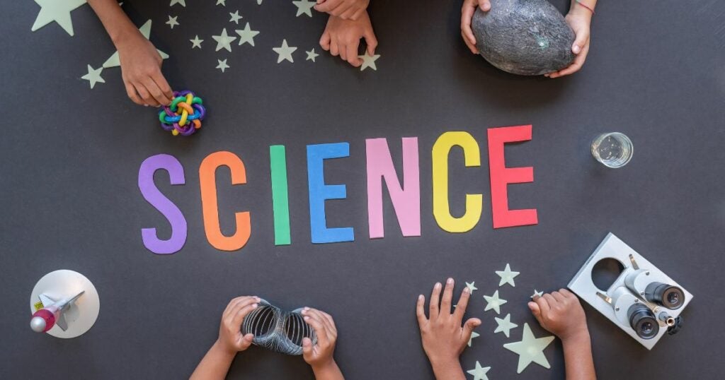 The text Science is written across a black floor using cutout paper.