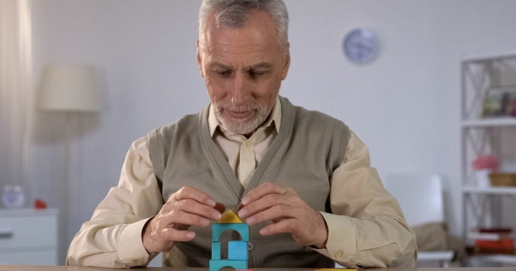 Image of an elderly man having problems with cognition. He is building a tower with building blocks.