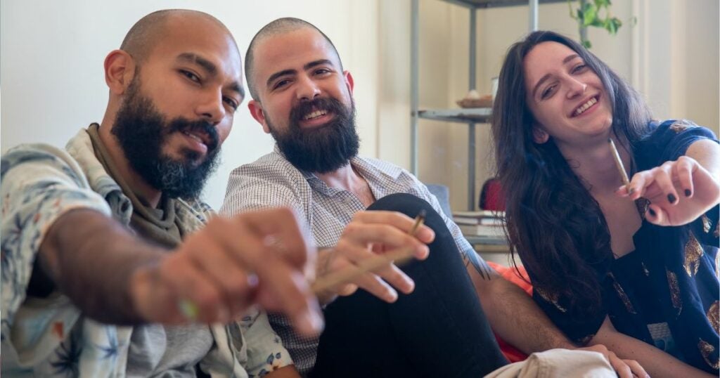 Three friends sitting on a couch. Each person has a joint in their hand.