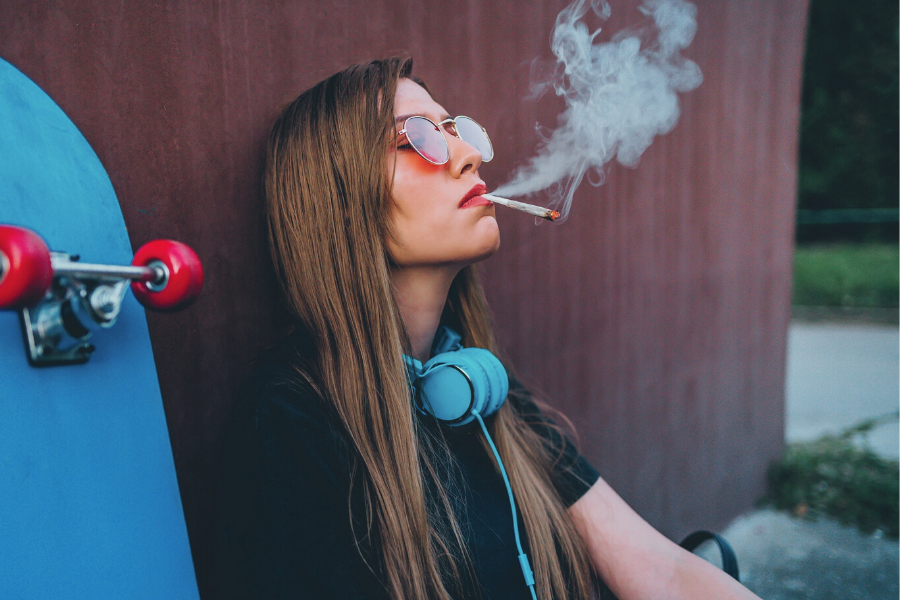 This image features a female smoking weed beside her blue skate board. How to get rid of weed smell.