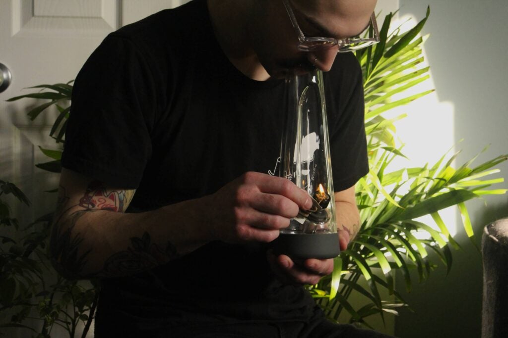 Young man with sunglasses smoking weed from a bong.