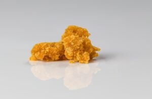Cannabis wax placed in front of a white background. It's orange, solid and looks like ear wax.