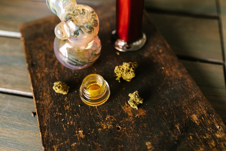 Various forms of cannabis placed on a brown table. There is a bong, flower and budder.