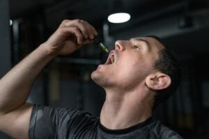 Young man ingesting CBD through a syringe. He is holding the syringe with one hand over his mouth.