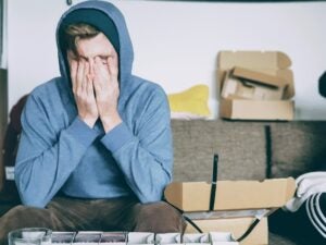 Young man in a blue hoodie covering his face in embarrassment.