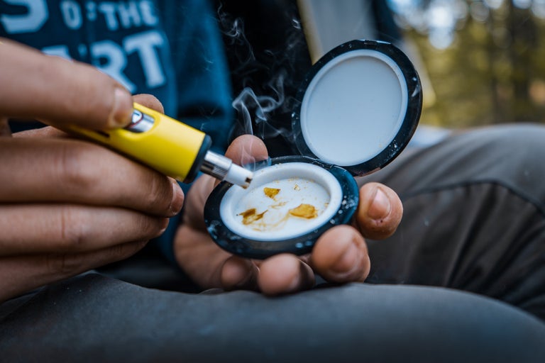 Young man heating up cannabis concentrates using a yellow dab pen.