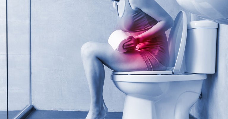 A young woman with digestive issues. She is sitting on a toilet bowl, holding her stomach. Her stomach is highlighted red to show her issues.