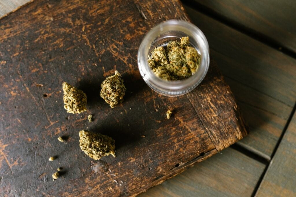 Cannabis buds in a grinder and wooden table.