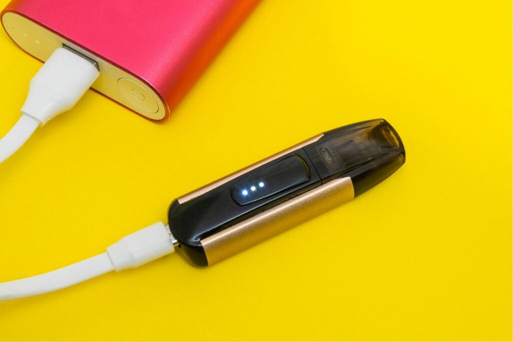 Charging gold and black THC Vape using a red portable charger.