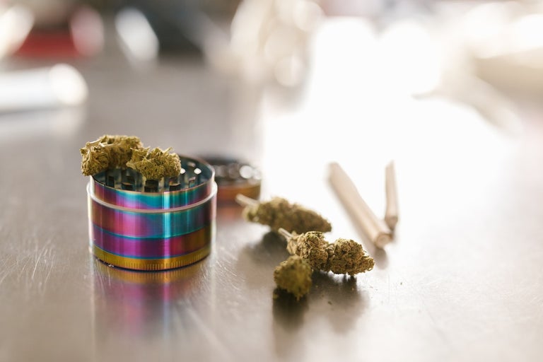 cannabis strain buds, two joints and a grinder sit on a metal table.