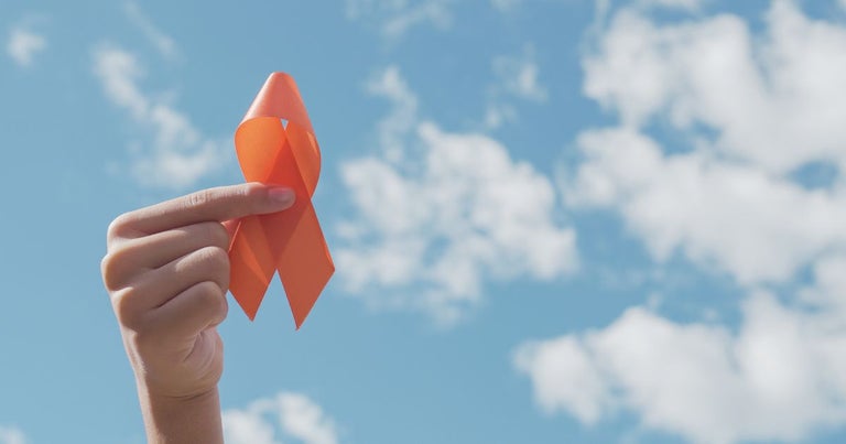 Ann orange ribbon that represents multiple sclerosis held up in front of the blue sky.