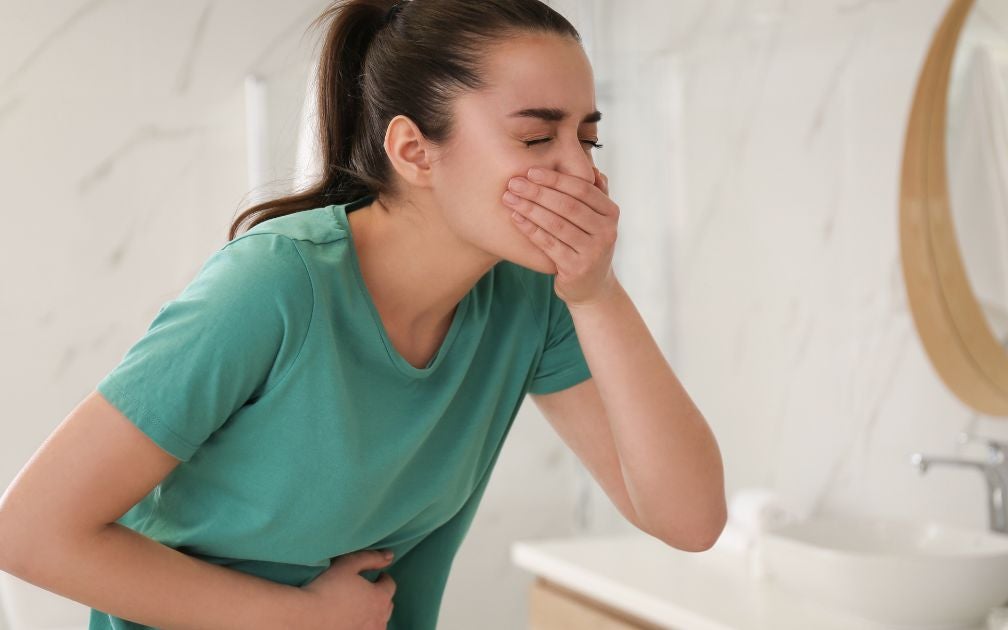 Young woman throwing up from chemotherapy-induced nausea. She is holding up her hand to cover her mouth and holding her stomach with the other.