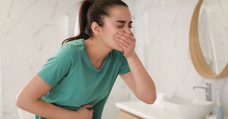 Young woman throwing up from chemotherapy-induced nausea. She is holding up her hand to cover her mouth and holding her stomach with the other.
