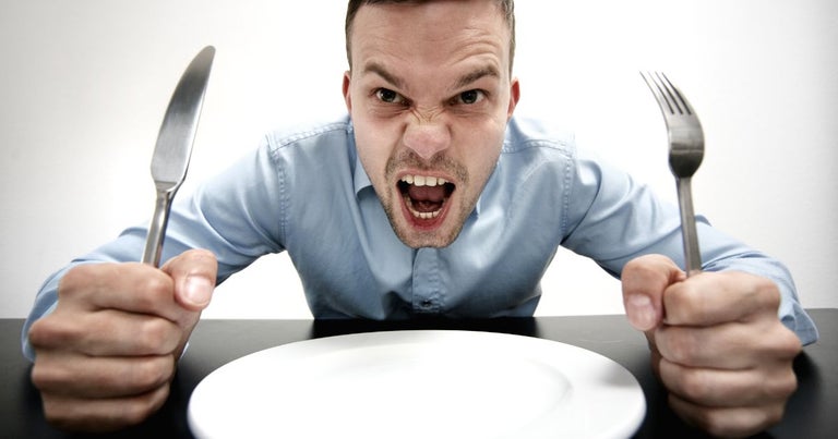 Young man with a fork and knife in each hand with an empty plate in front of him. He is clearly dissatisfied with the lack of food.