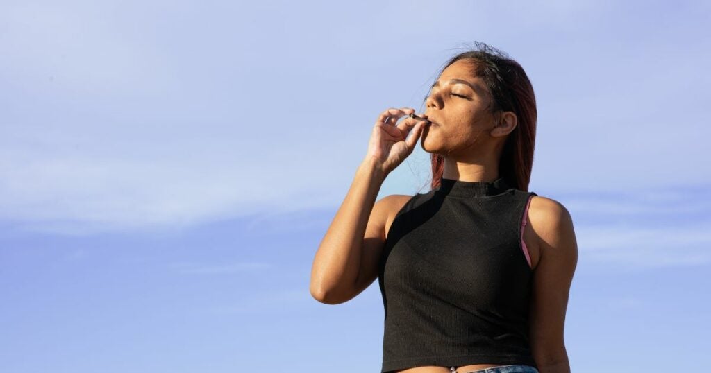 Young woman smoking a cannabis joint on a clear blue sky day.